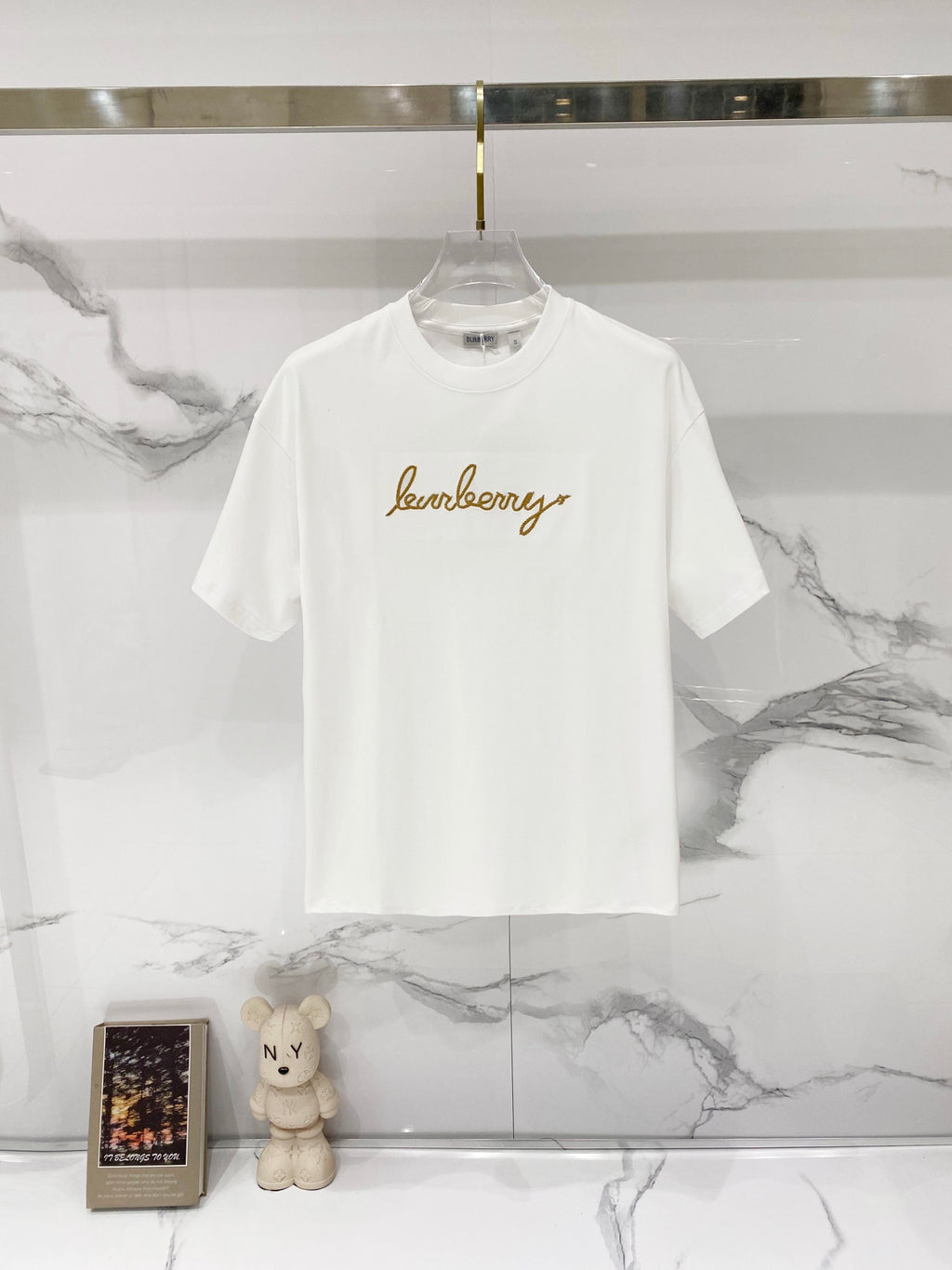 White short-sleeve T-shirt with gold logo text graphic on the chest