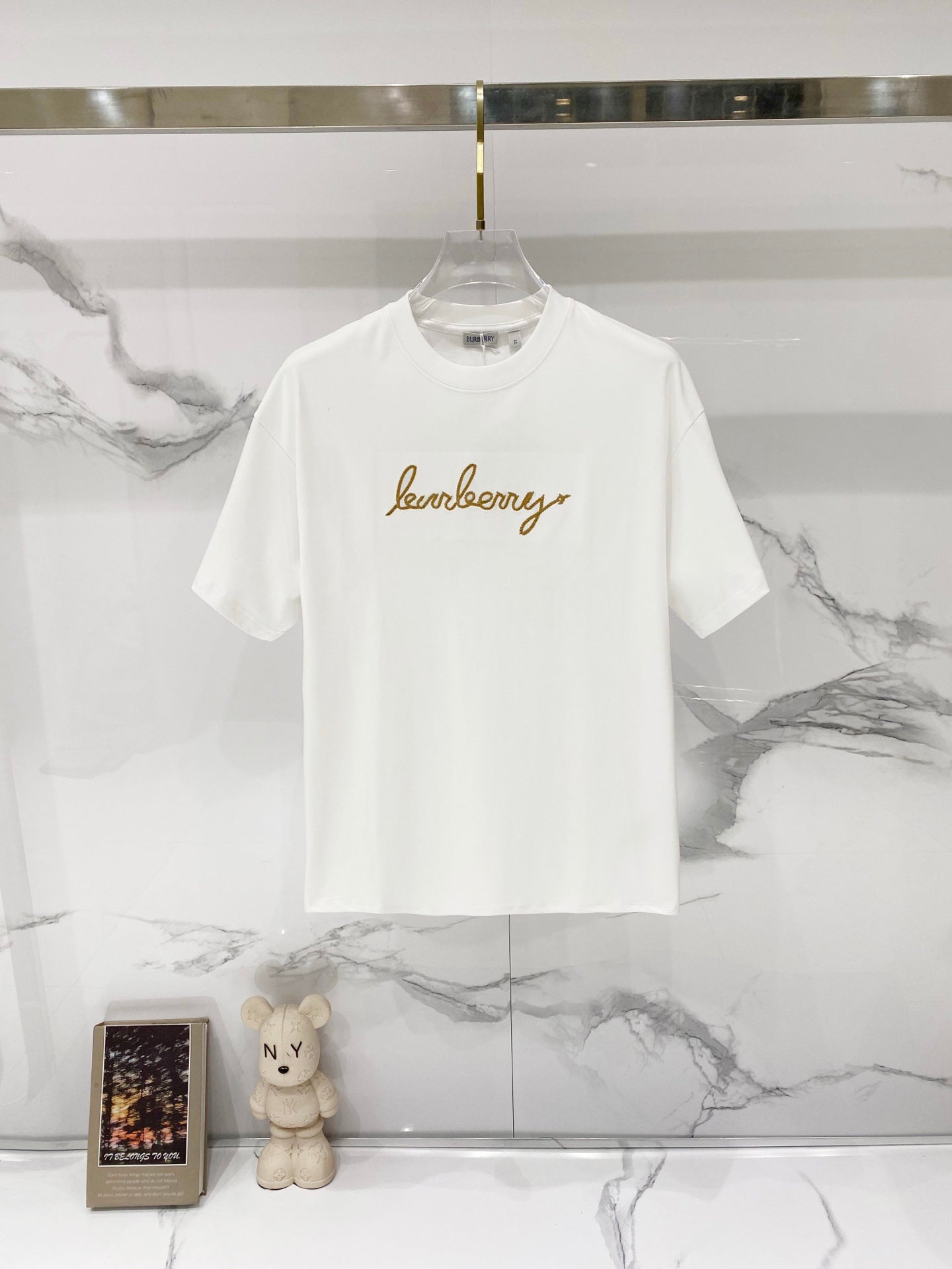 White short-sleeve T-shirt with gold logo text graphic on the chest