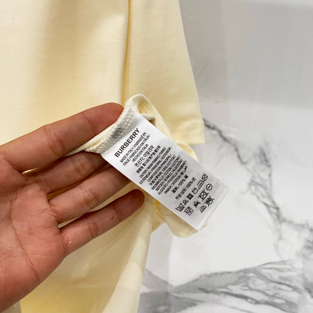 Burberry T-shirt care label on pale cream fabric, held in hand