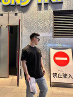 Black short-sleeve T-shirt with tan logo patch, model standing in profile