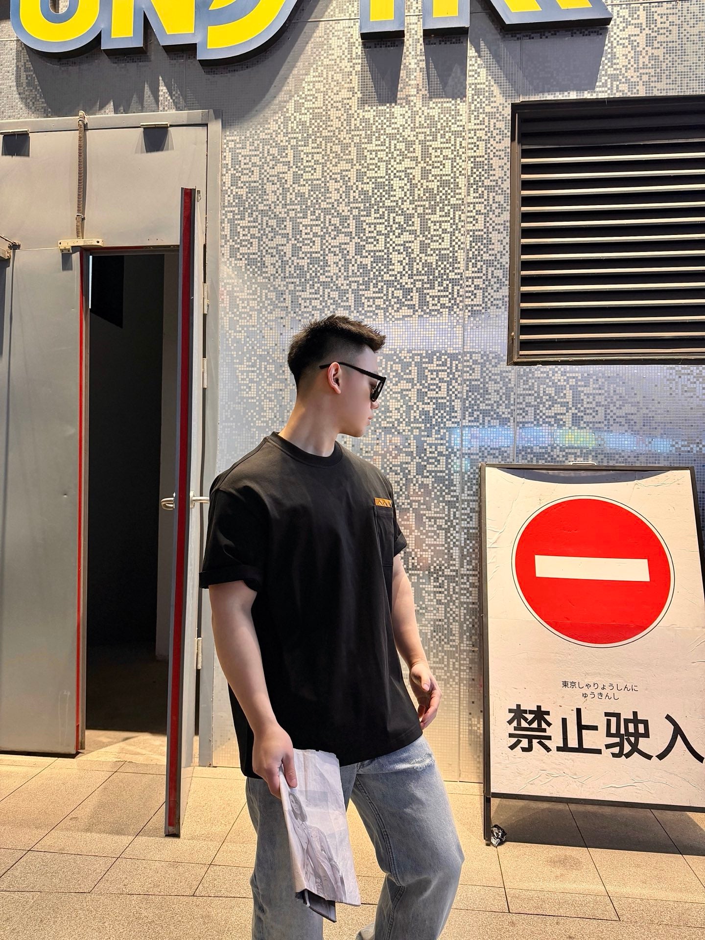Black short-sleeve T-shirt with tan logo patch, model standing in profile