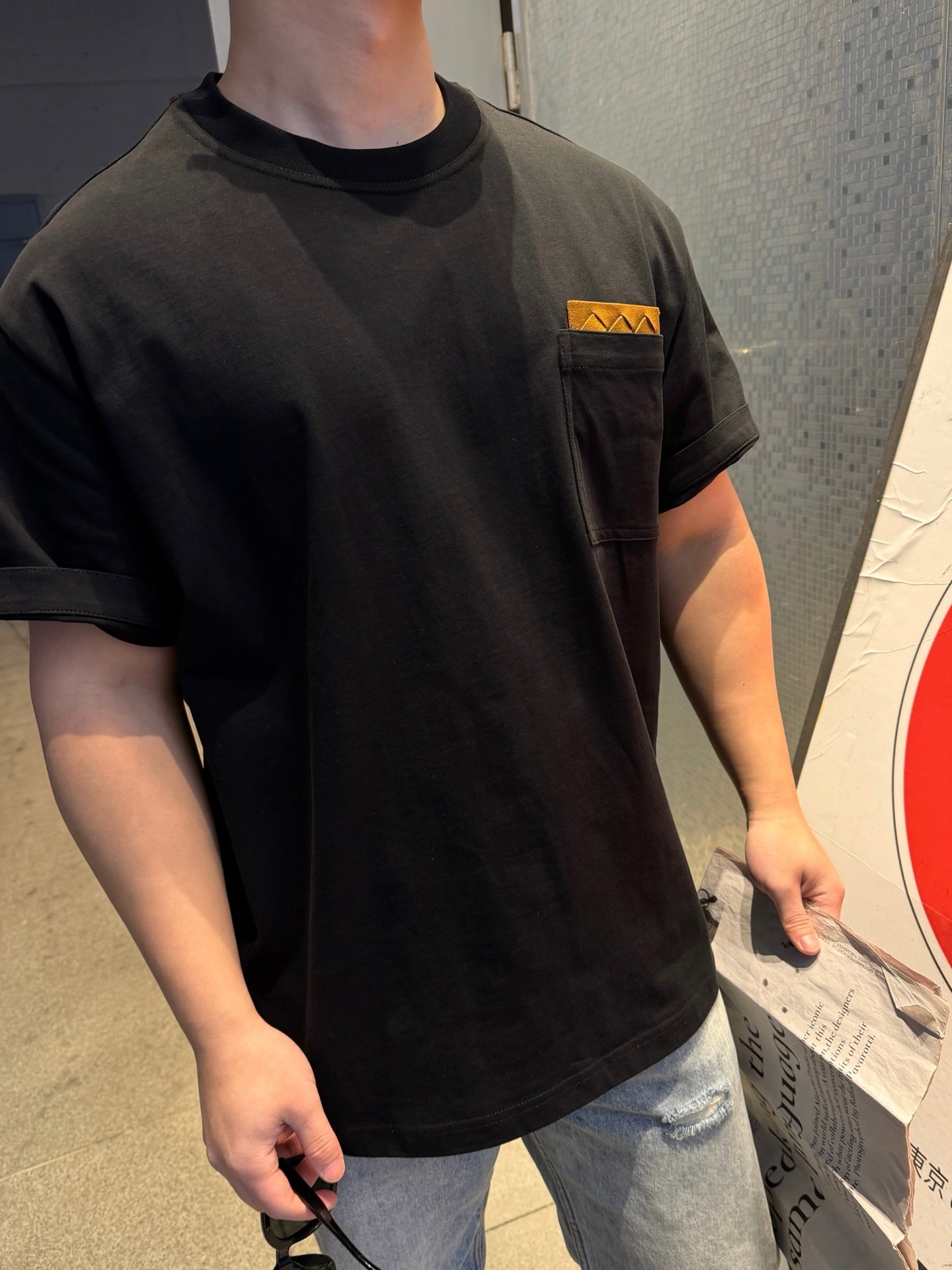 Black short-sleeve T-shirt close-up, tan logo patch on chest, crew neck