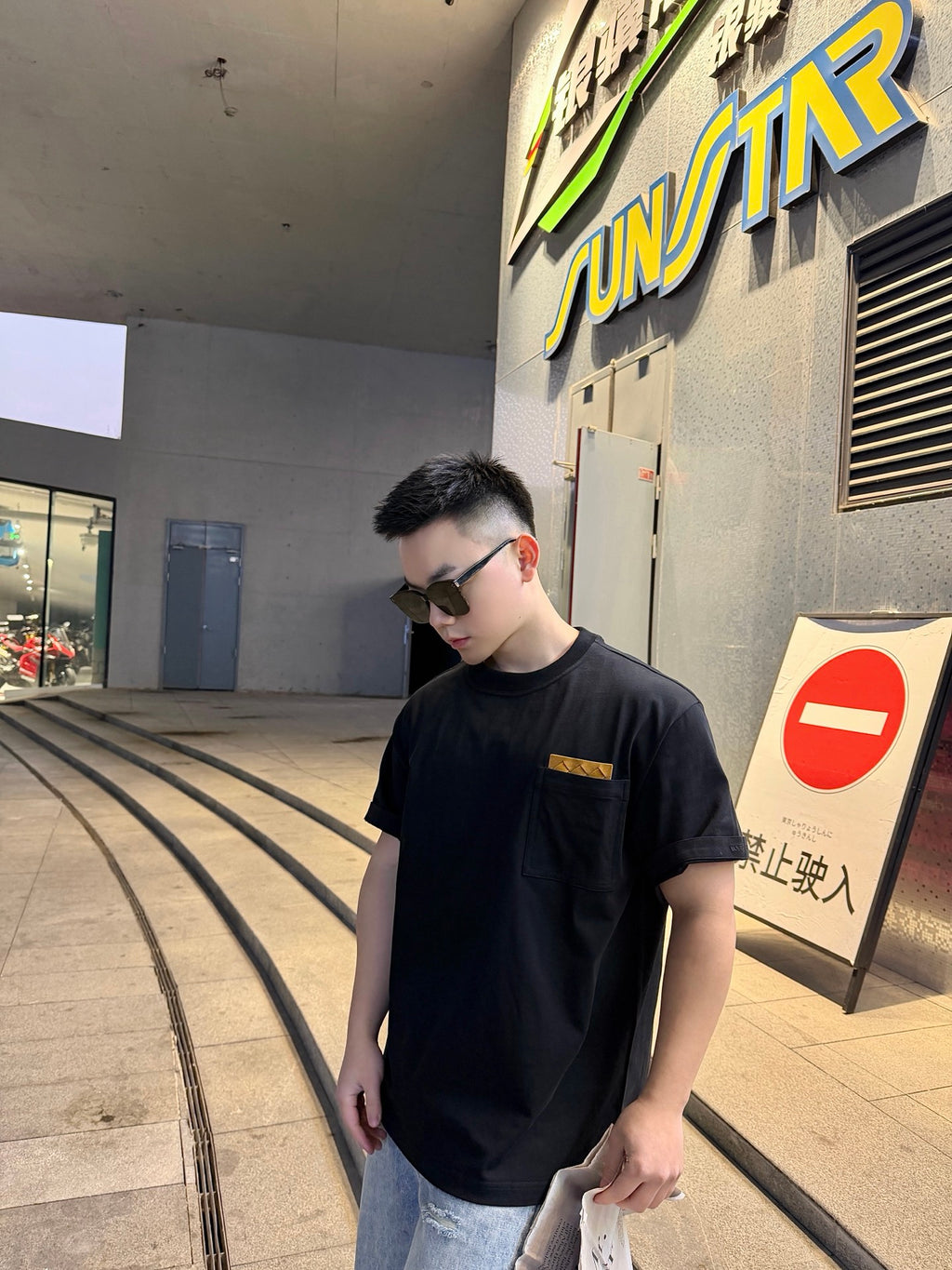 Black short-sleeve T-shirt with tan logo patch, front view, model wearing jeans