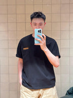 Black short-sleeve T-shirt with tan logo patch, crew neck, front mirror selfie