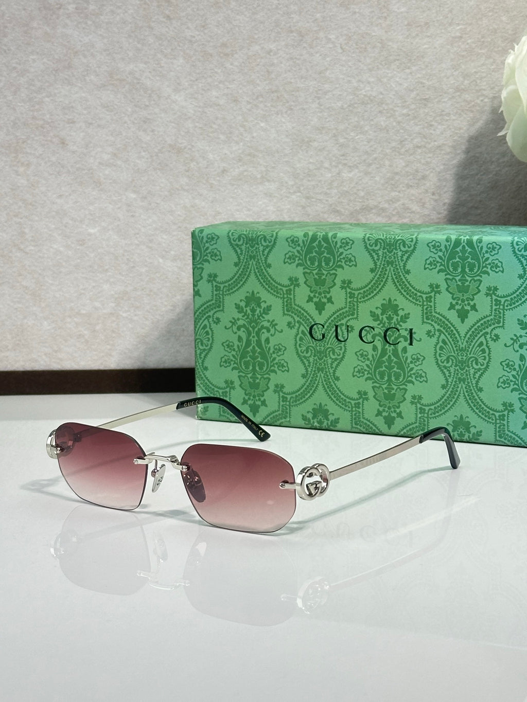 Gold-framed sunglasses with pink-tinted lenses and green temple accents