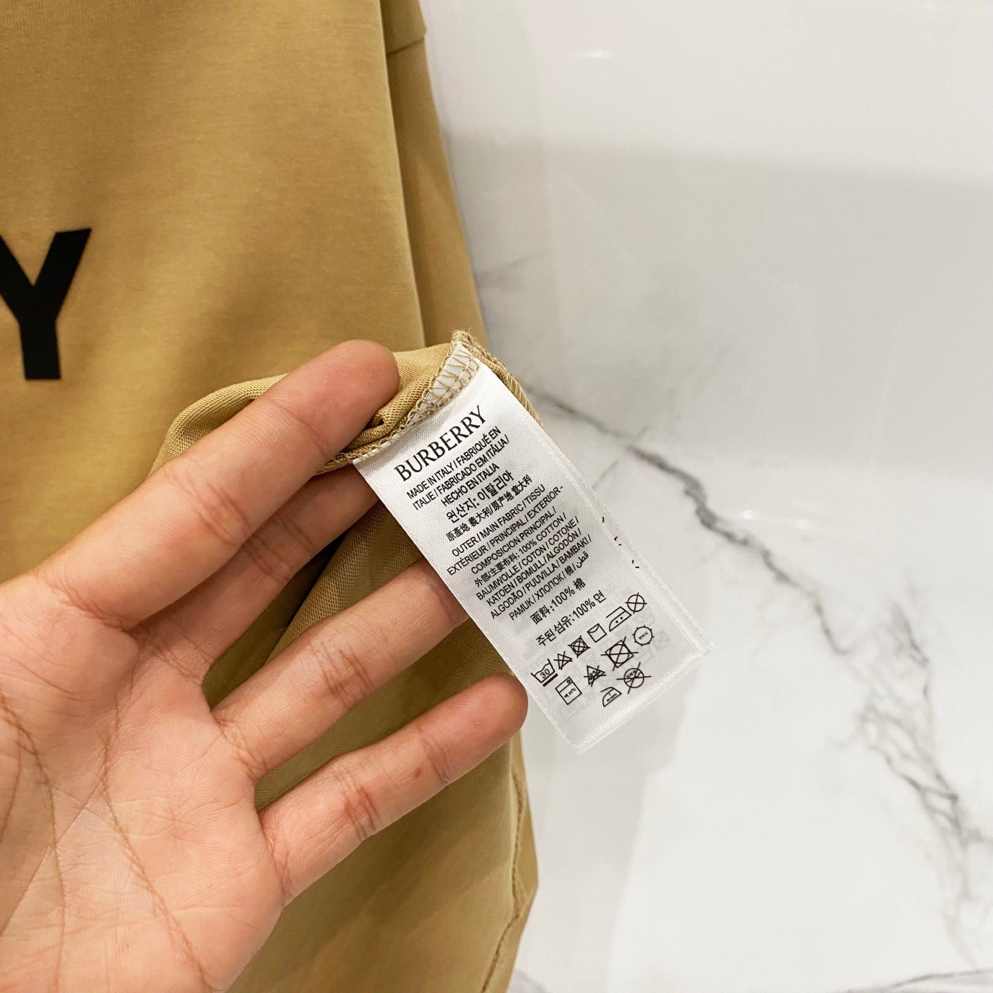 Burberry tan T-shirt fabric tag and care label held in a hand