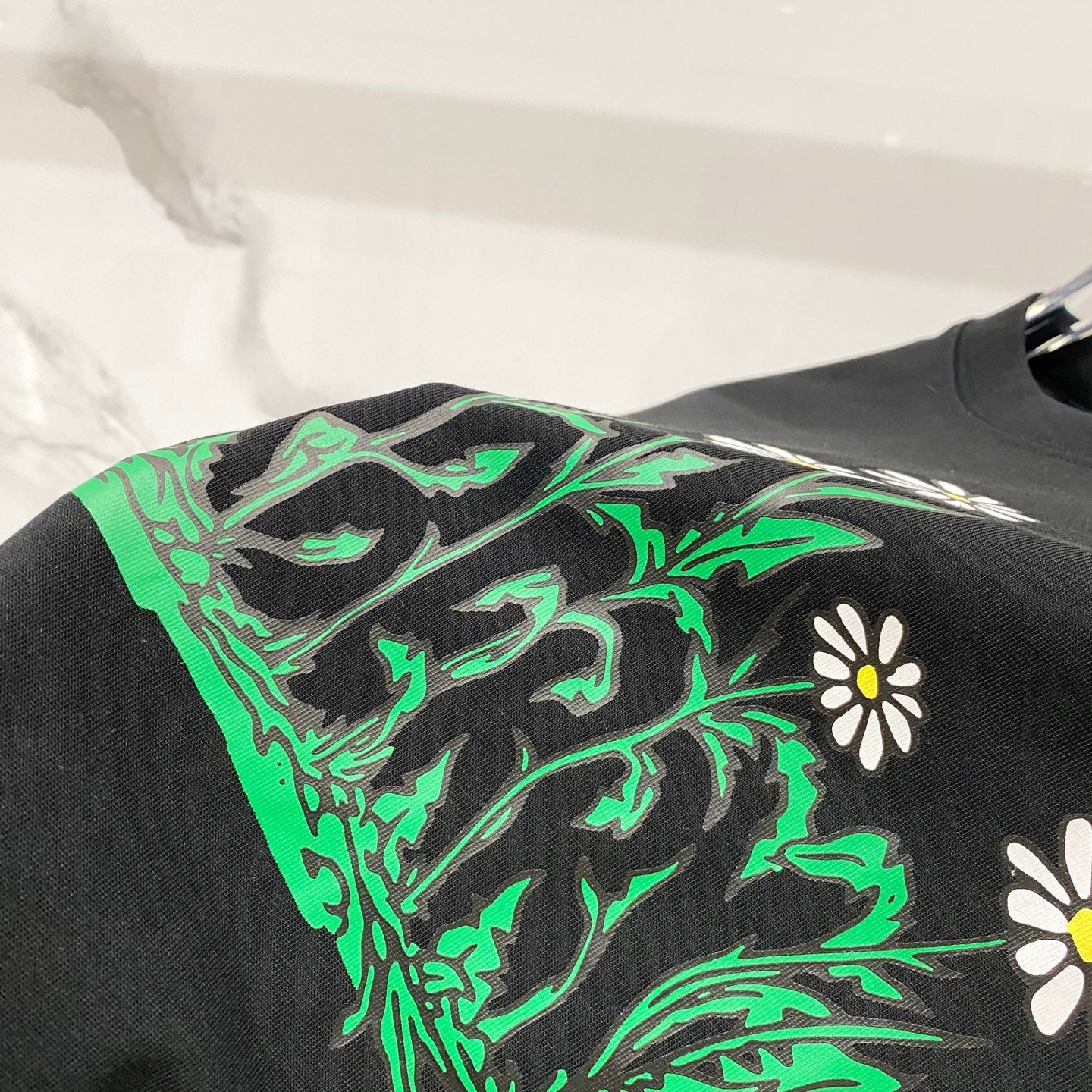 Black Burberry T-shirt graphic closeup with green foliage and daisies