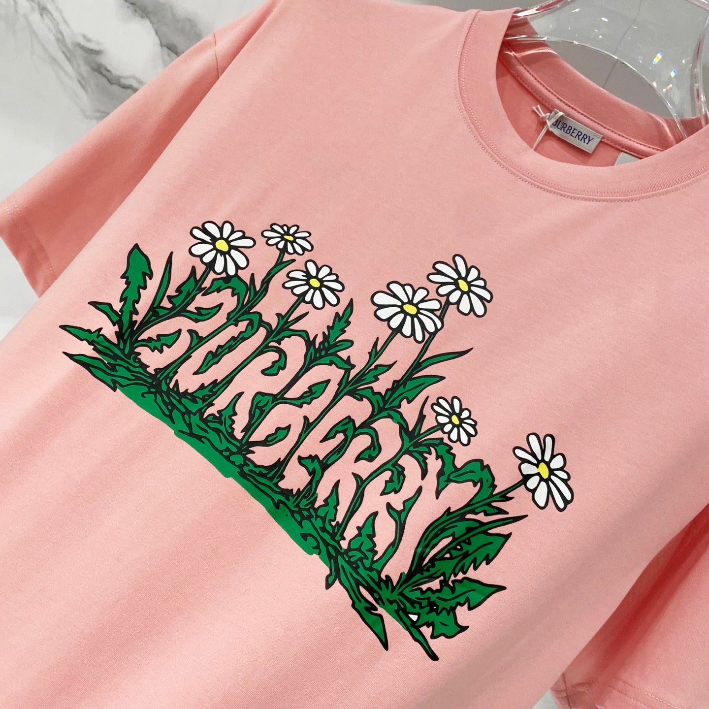 Pink Burberry T-shirt with colorful daisy and green foliage graphic.