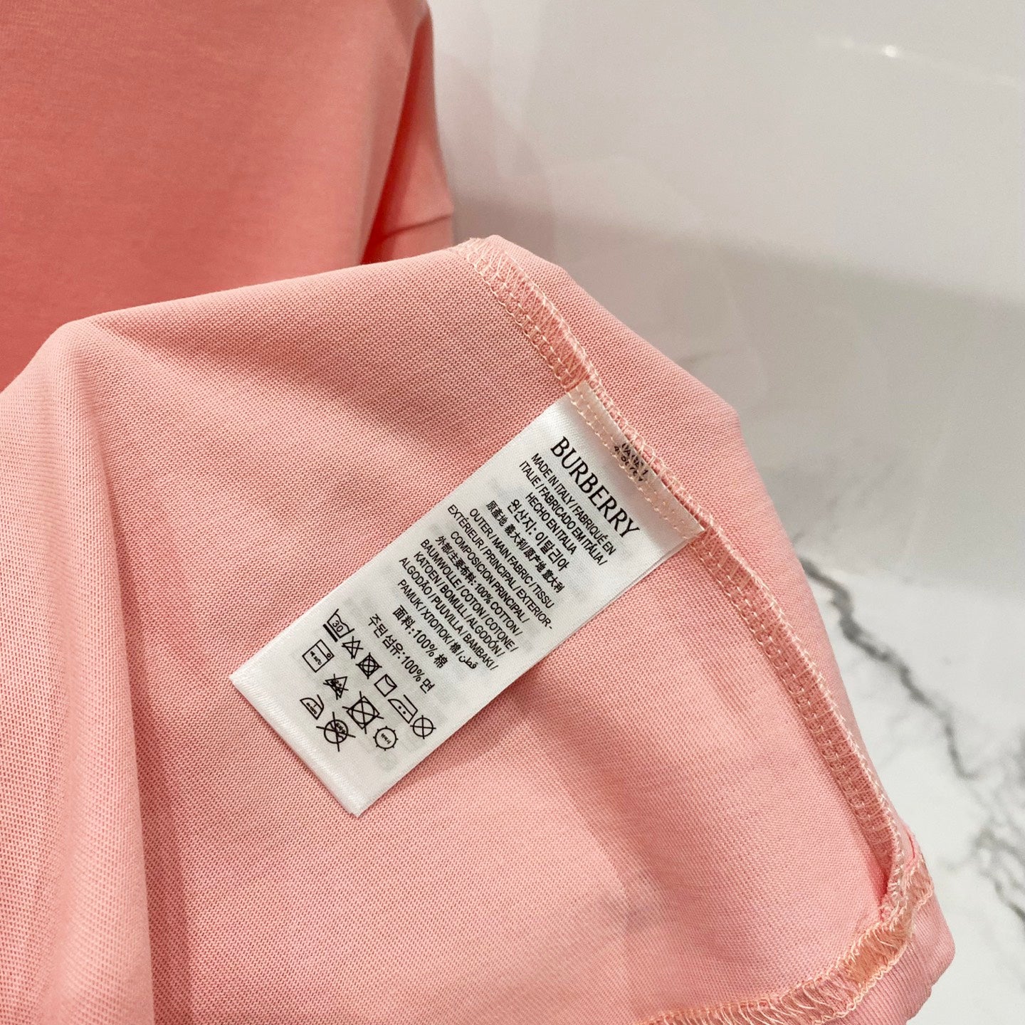 Pink Burberry T-shirt care label on the sleeve edge.