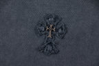 Close-up of dark embroidered cross-like emblem with gold-toned center.