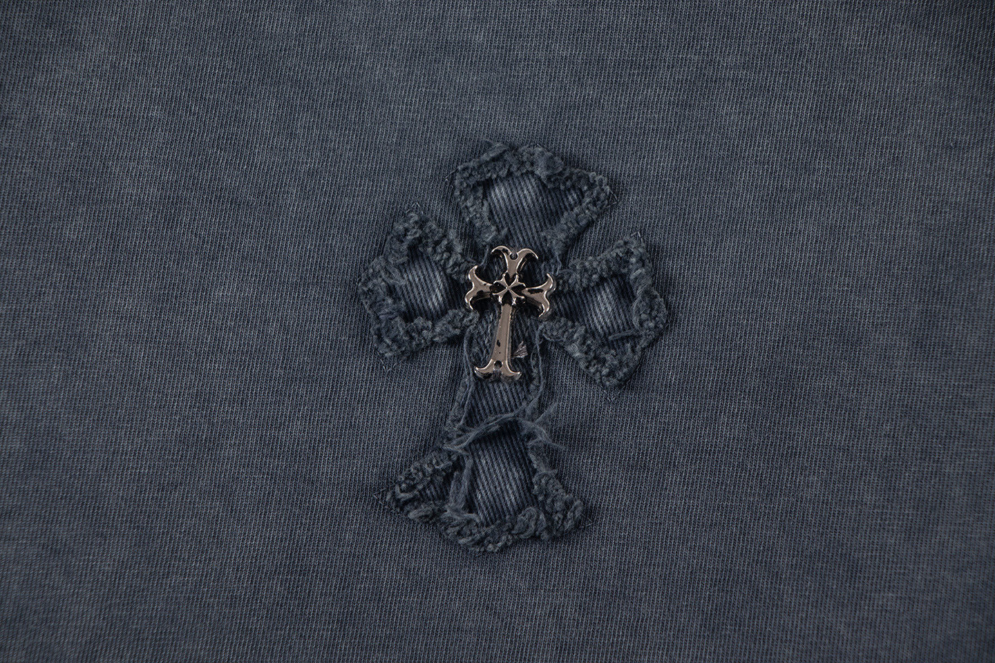 Close-up of dark embroidered cross-like emblem with gold-toned center.