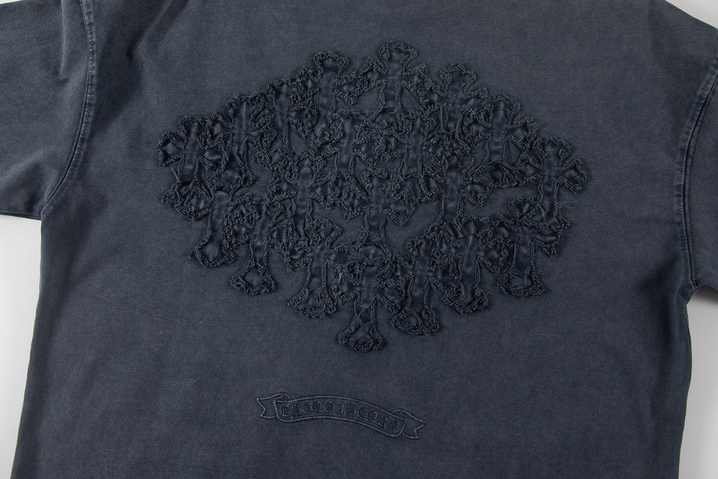 Dark T-shirt front with large embroidered graphic and small chest emblem.
