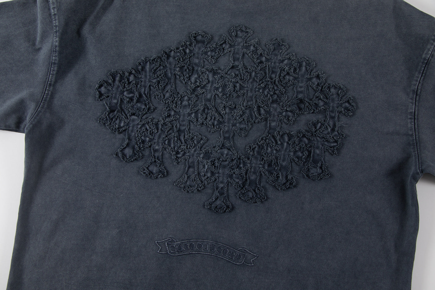 Dark T-shirt front with large embroidered graphic and small chest emblem.