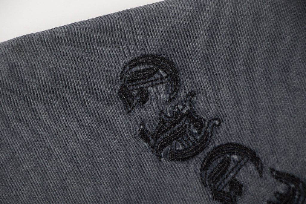 Close-up of dark gray graphic T-shirt fabric with embroidered symbol on sleeve