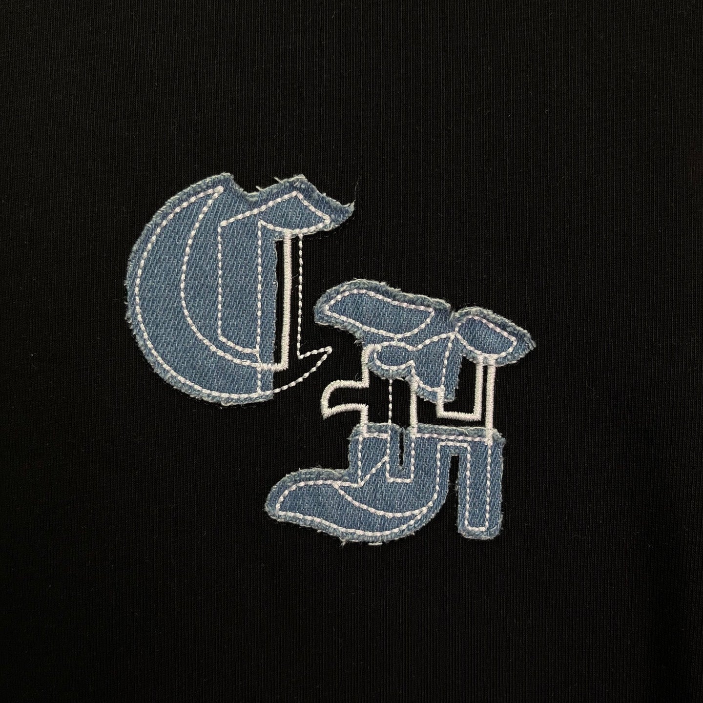 Black T-shirt close-up with embroidered light-blue logo detail