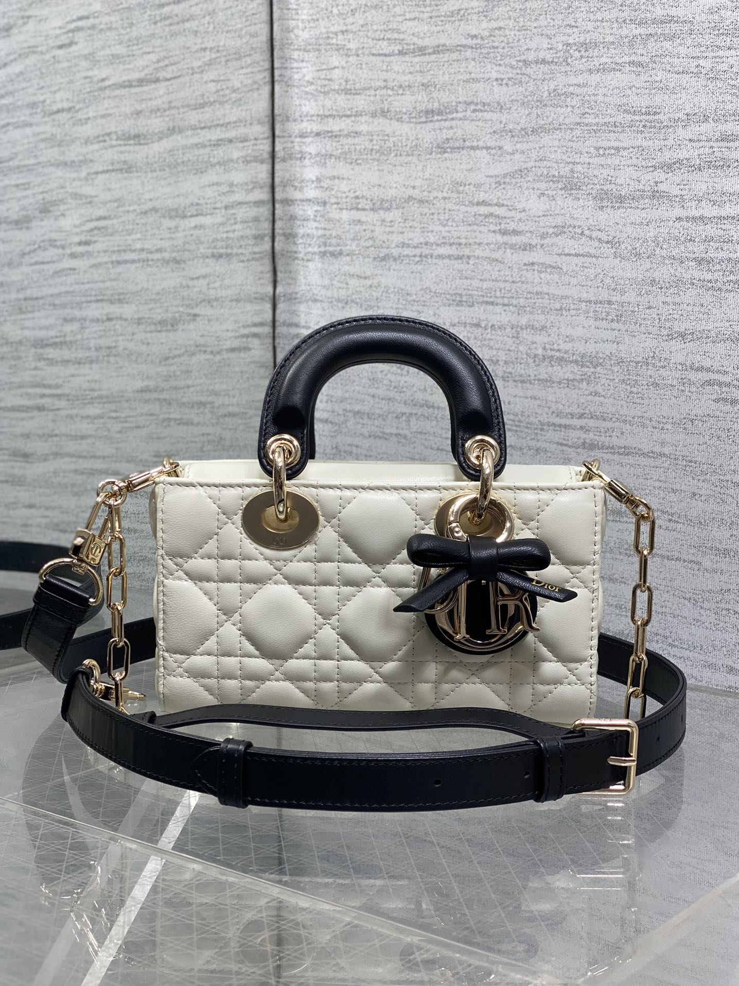 Quilted handbag with black leather top handles, bow emblem, and gold chain accents