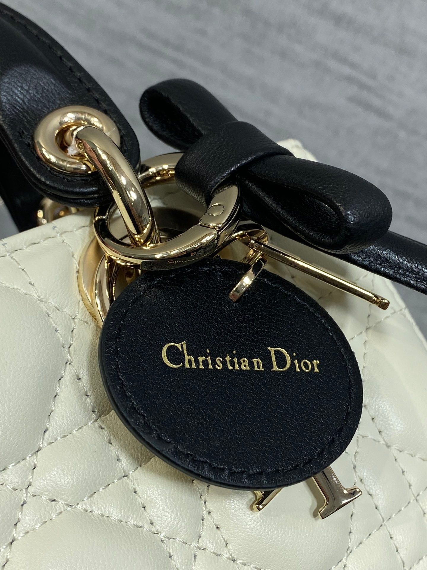 Quilted handbag charm tag reading "Christian Dior" with gold hardware and black bow