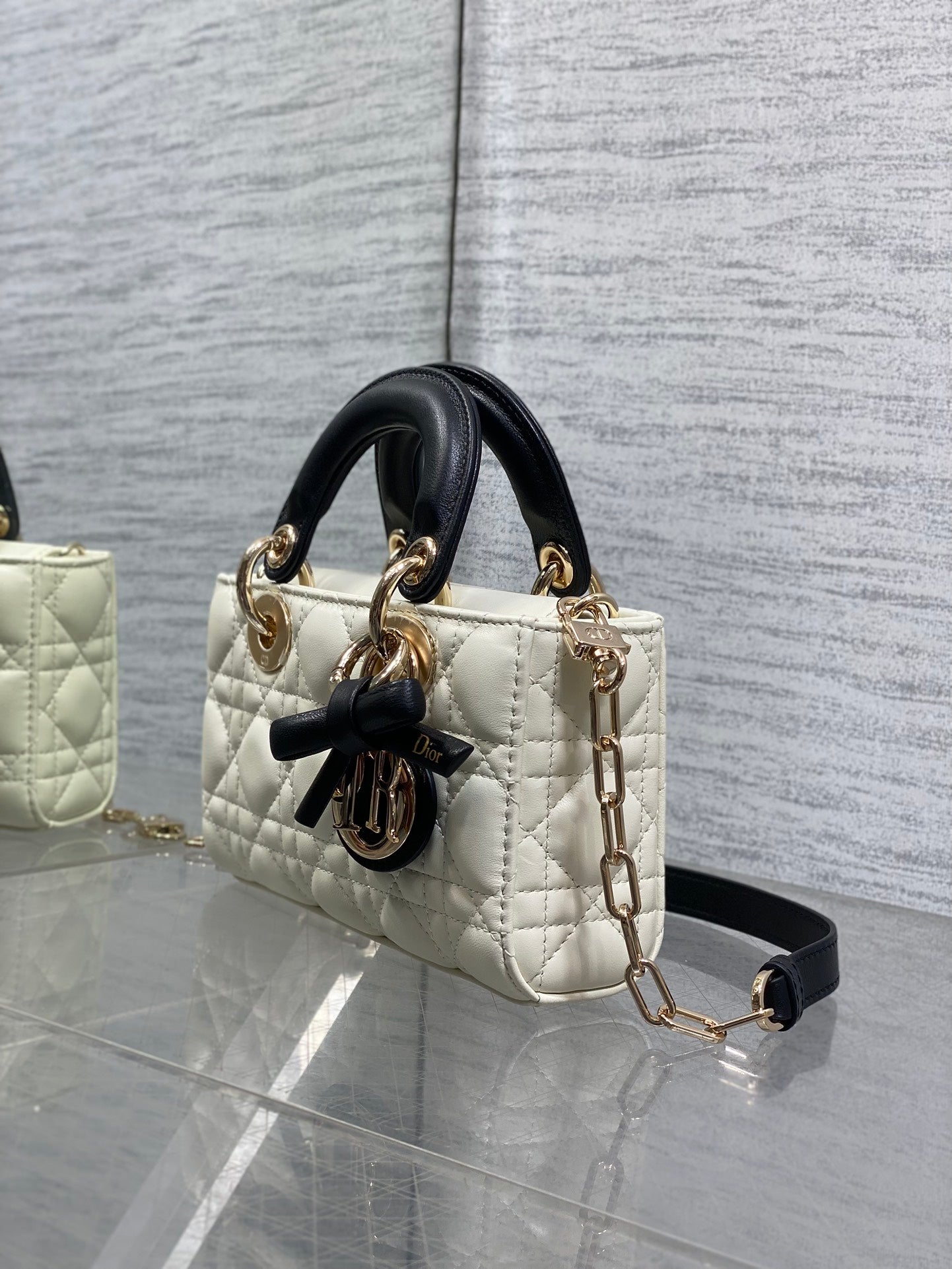 Quilted handbag angled view with black handles, bow emblem, and gold-tone chain strap
