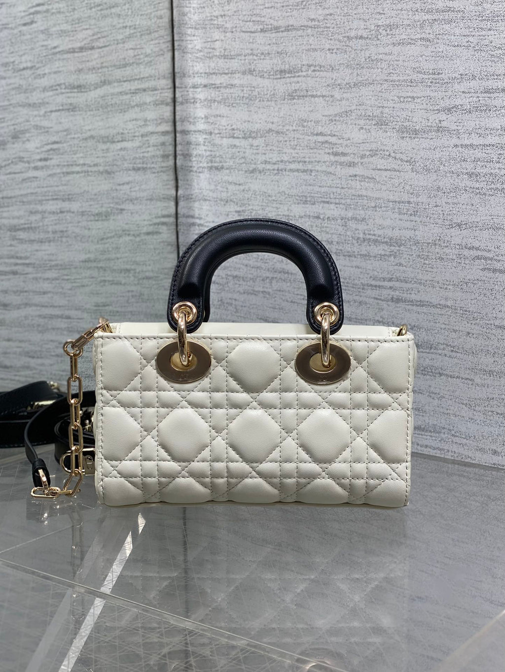 Quilted handbag with black leather handles, white body, and gold-tone rings at top