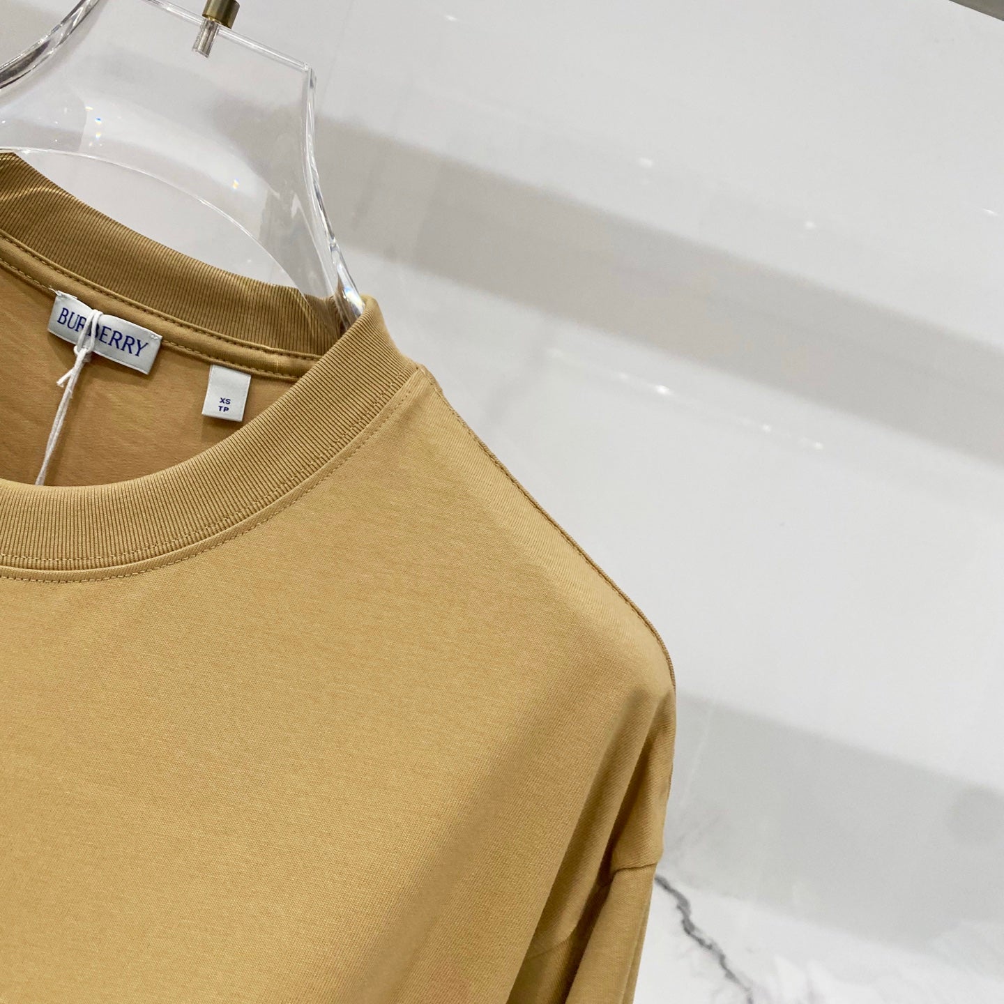 Tan short-sleeve T-shirt shoulder and sleeve detail on clear hanger
