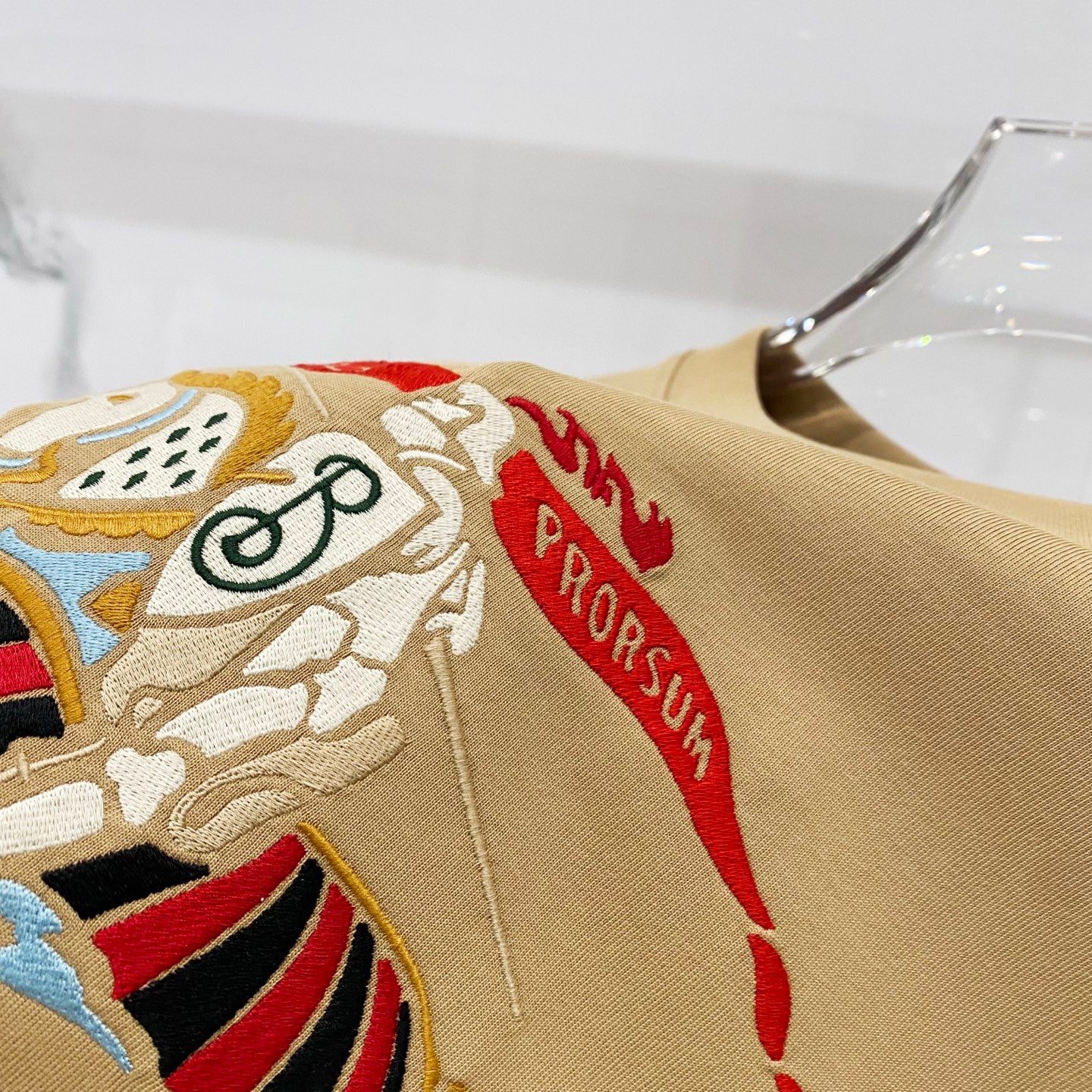 Tan T-shirt close-up with embroidered cartoon horse and red banner details