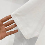 White T-shirt held by hand, showing hem edge and side seam stitching