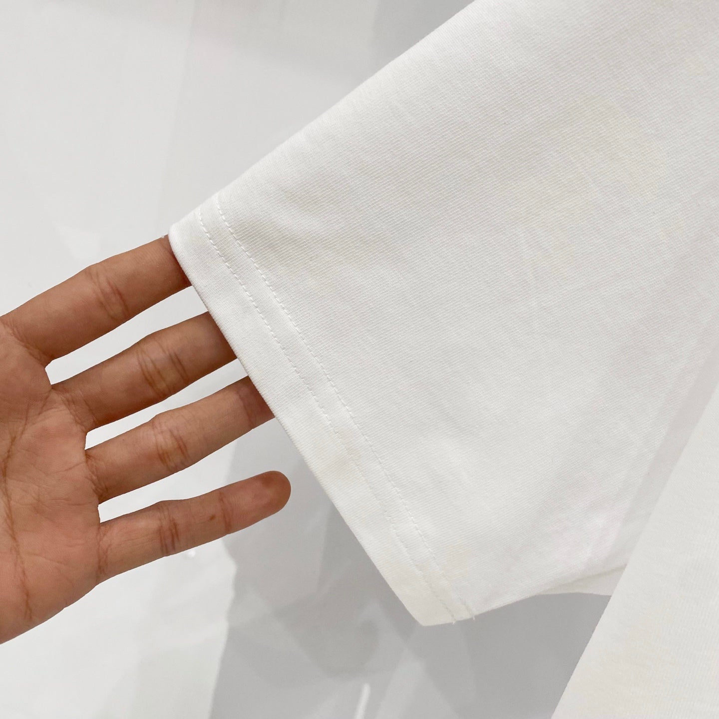 White T-shirt held by hand, showing hem edge and side seam stitching