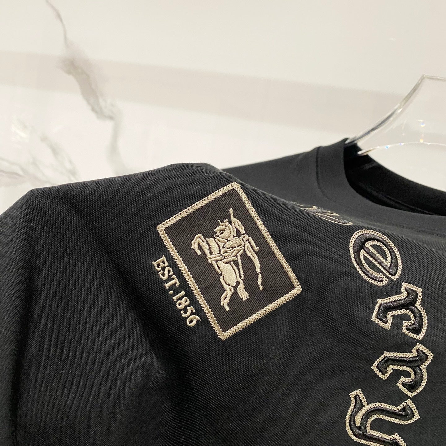 Black T-shirt with gold crest patch and EST.1885 embroidery detail