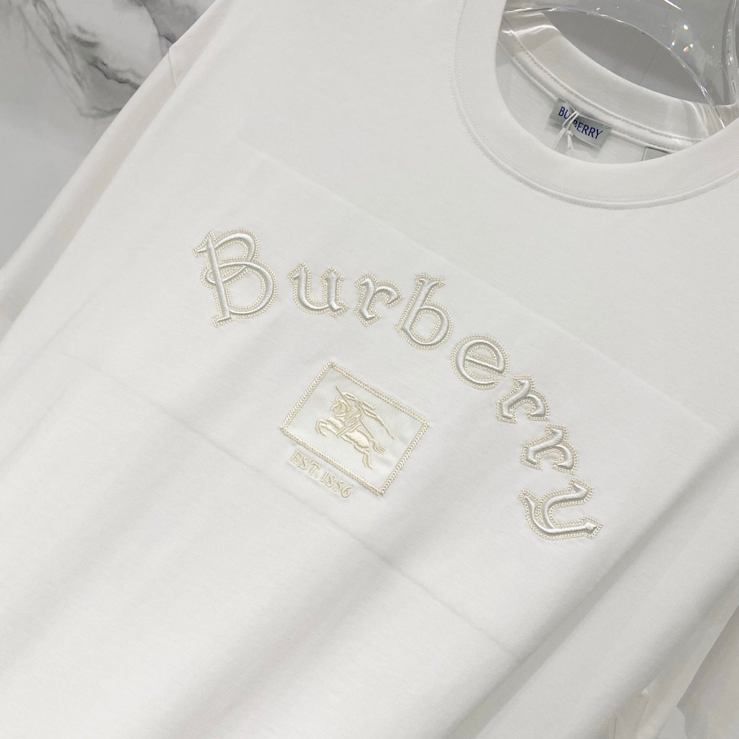 White T-shirt front with “Burberry” text-style embroidery and small crest patch