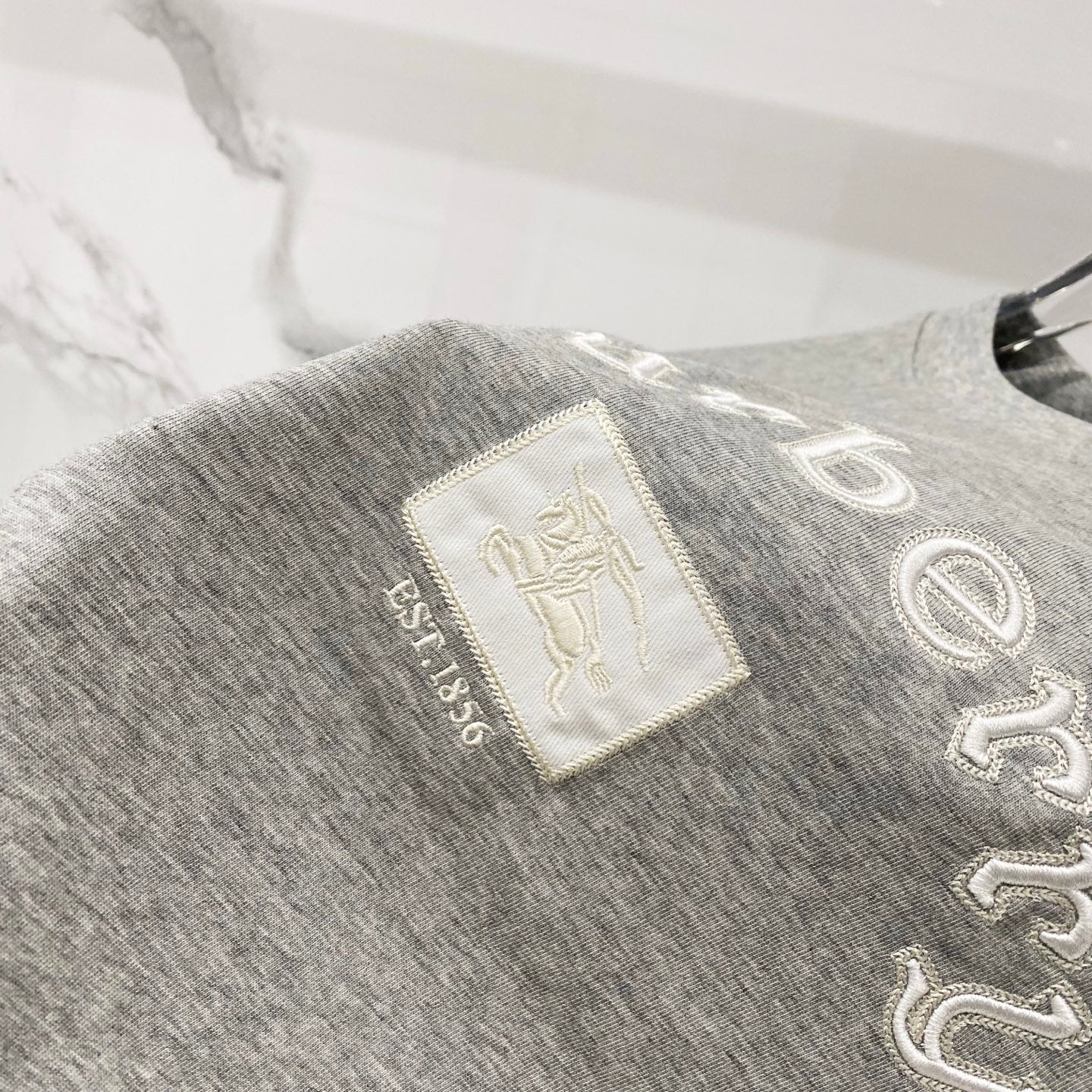 Grey T-shirt with embroidered “Burberry” text and small logo patch detail