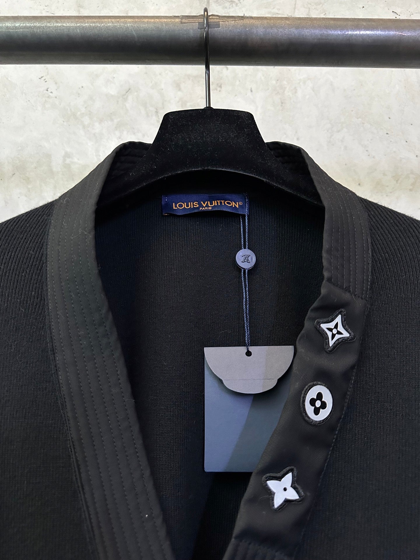 Black long coat collar close-up with Louis Vuitton hang tag and lapel icon pins
