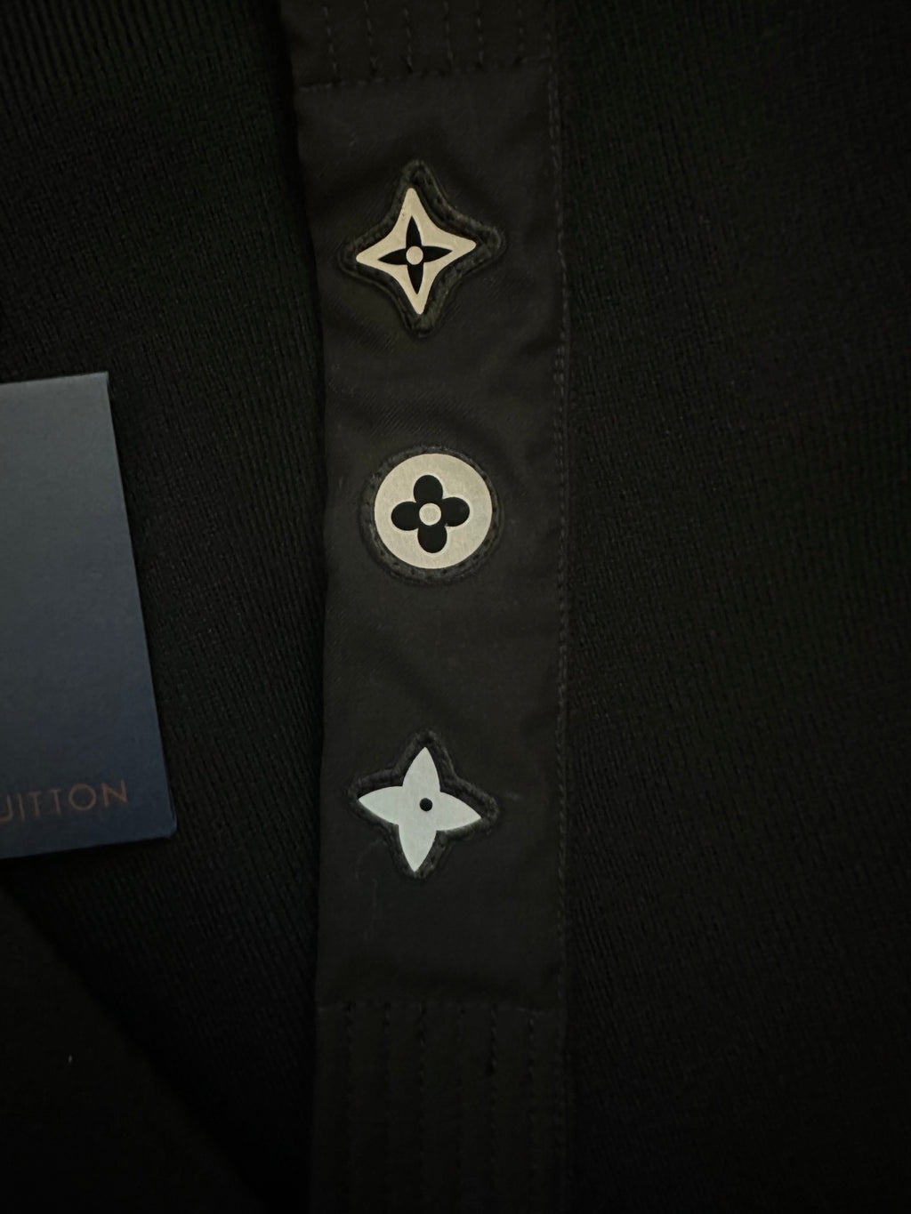 Black long coat front placket close-up with embroidered star and flower icons