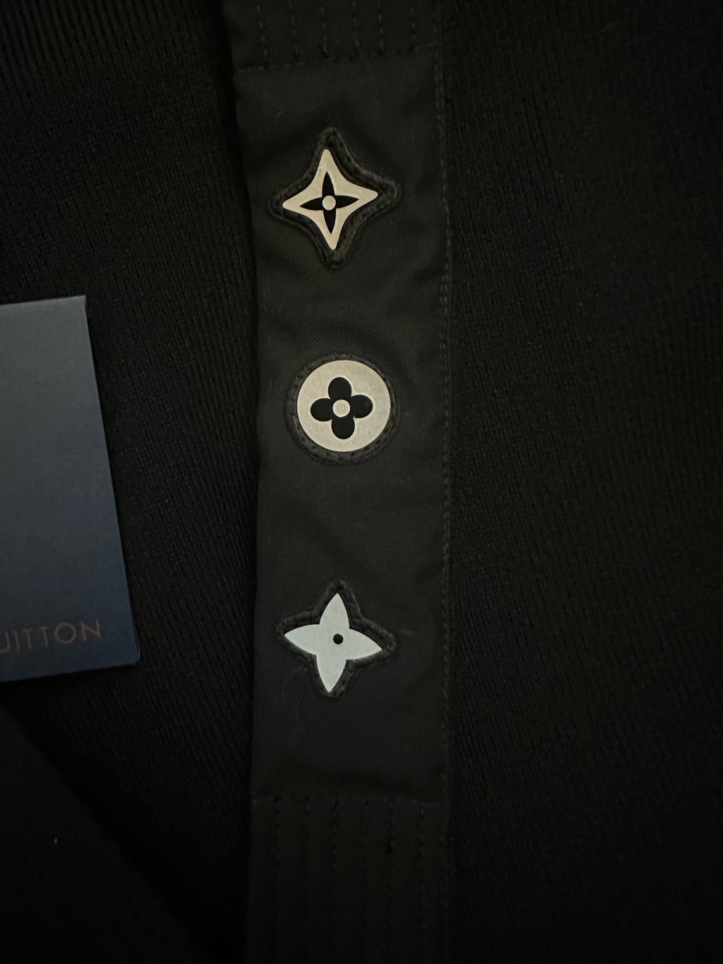 Black long coat front placket close-up with embroidered star and flower icons