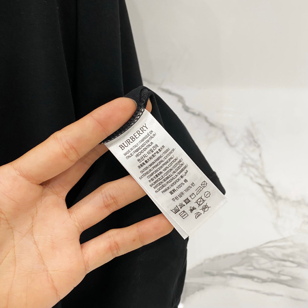 Black T-shirt care label tag with printed text on the inside neck.