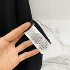 Black T-shirt care label tag with printed text on the inside neck.