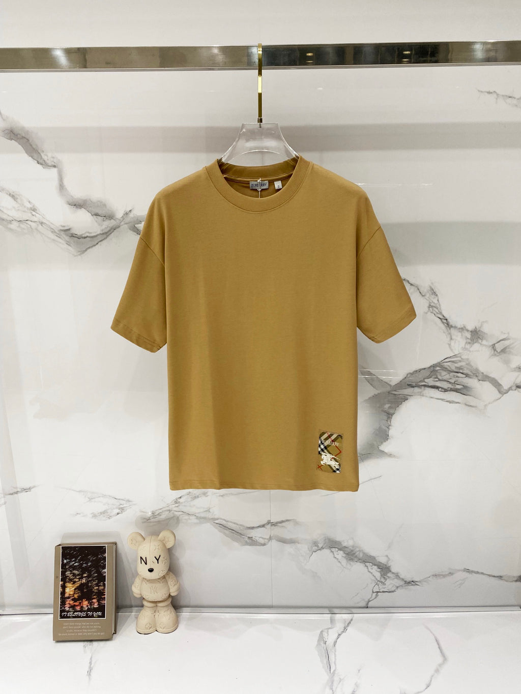 Tan crew-neck short-sleeve T-shirt with small logo graphic at hem
