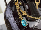Louis Vuitton bag detail: gold chain charm with blue gemstone and monogram pattern on glossy finish.