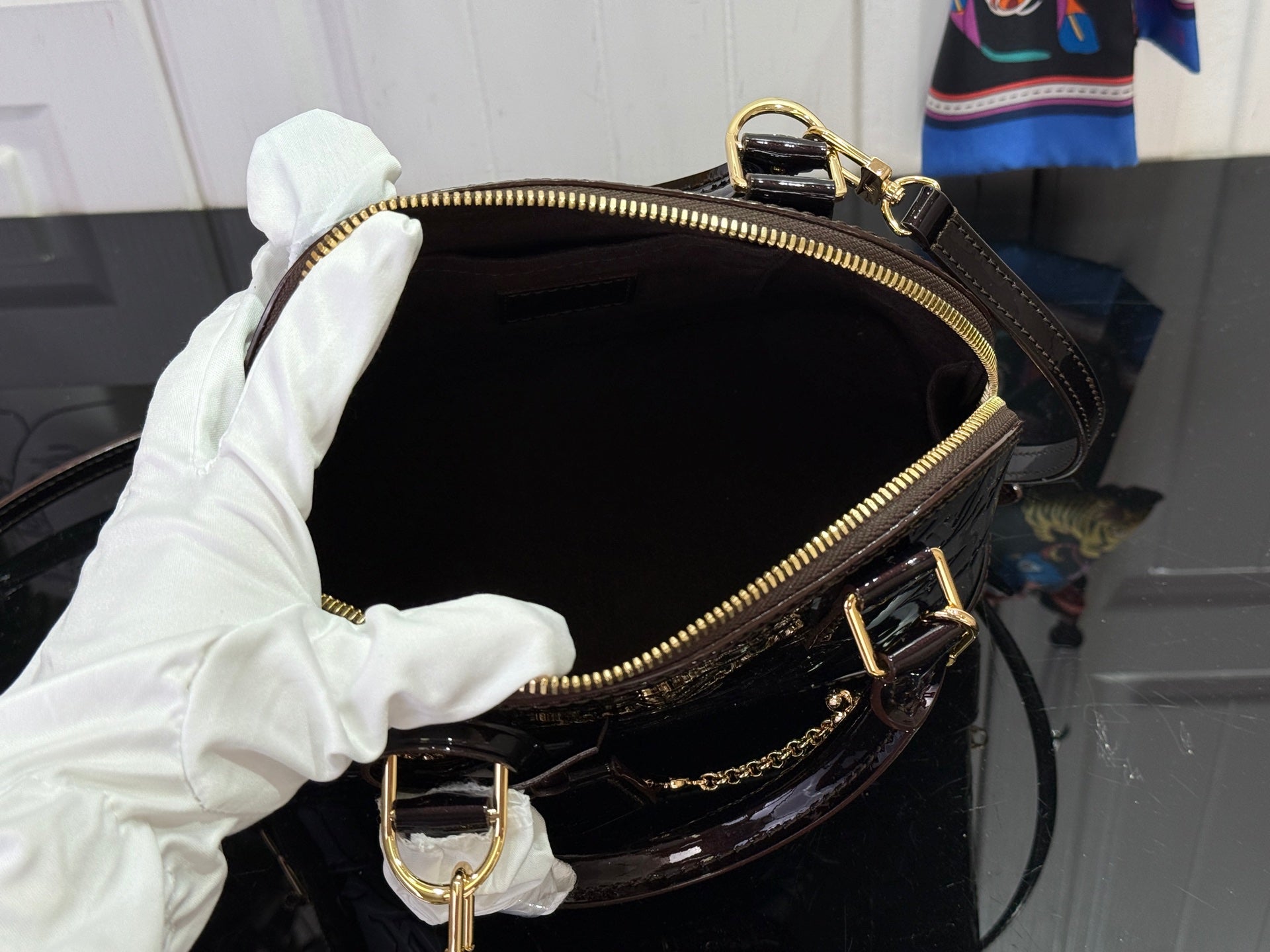 Louis Vuitton bag open top with dark interior, zipper closure, gold trim, and chain strap.