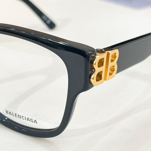 Balenciaga eyeglasses close-up: dark navy frame with gold B hinge detail
