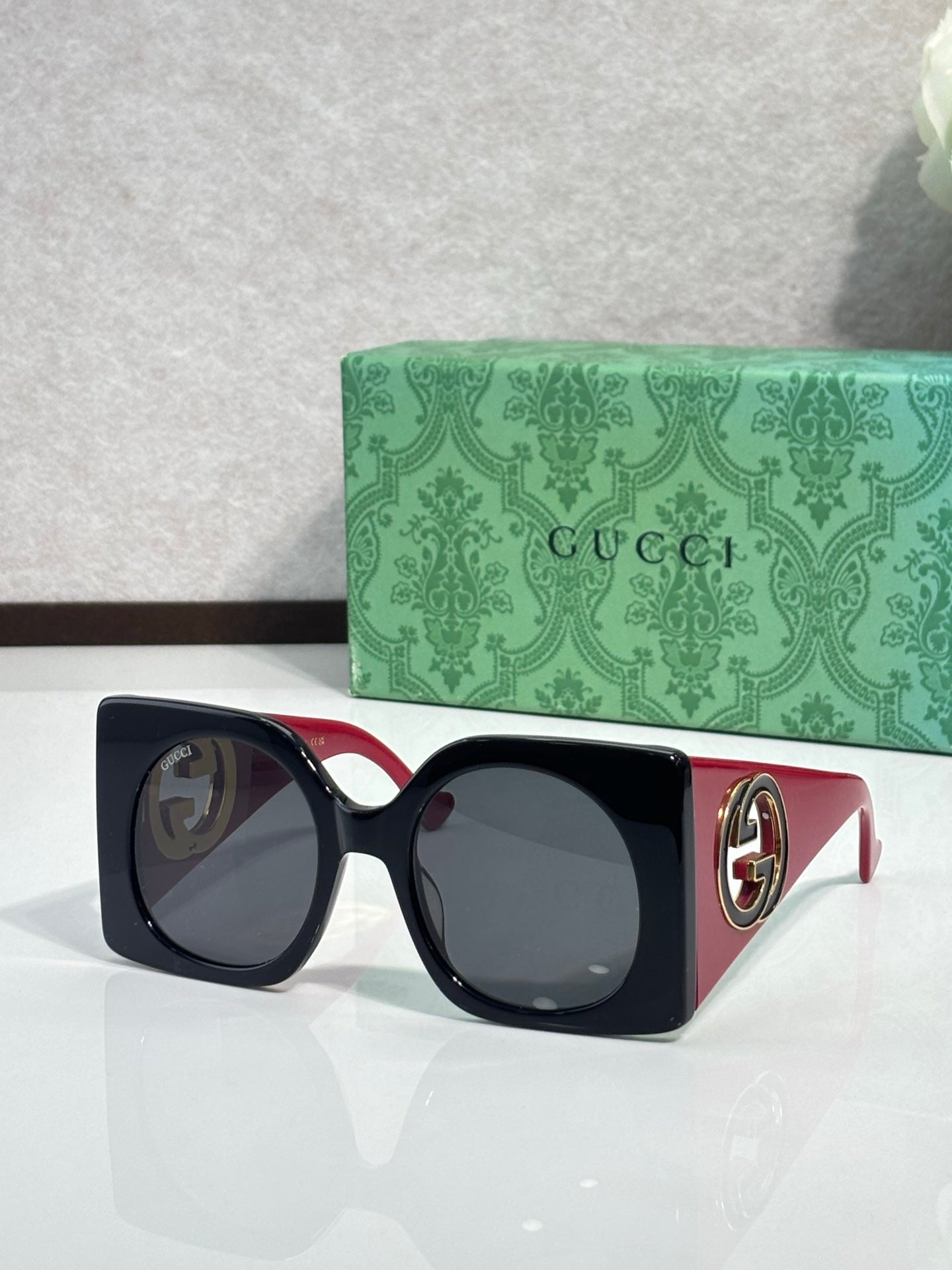 Gucci sunglasses with black square frames and dark tinted lenses, red temple accents