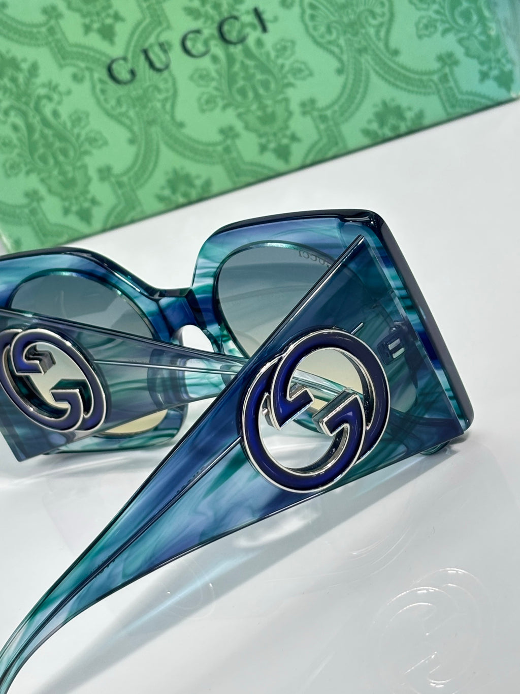 Gucci sunglasses close-up with blue transparent frames and tinted lenses, metal G logo