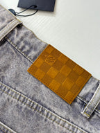 Close-up of light blue denim pants with tan checkered logo patch on front pocket