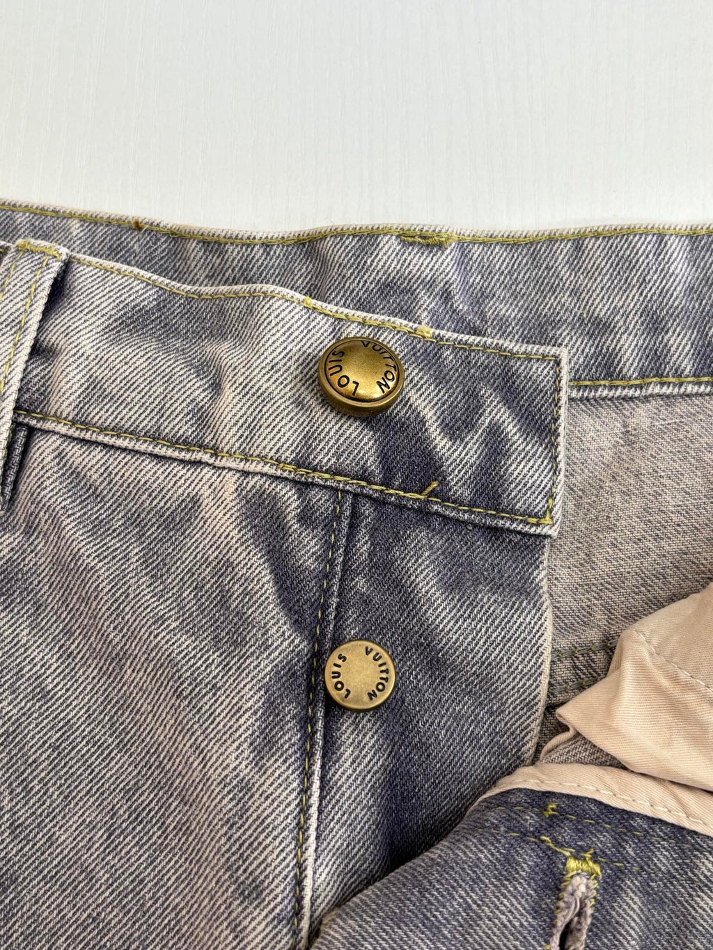 Close-up of light blue denim pants back pockets with gold-toned button accents