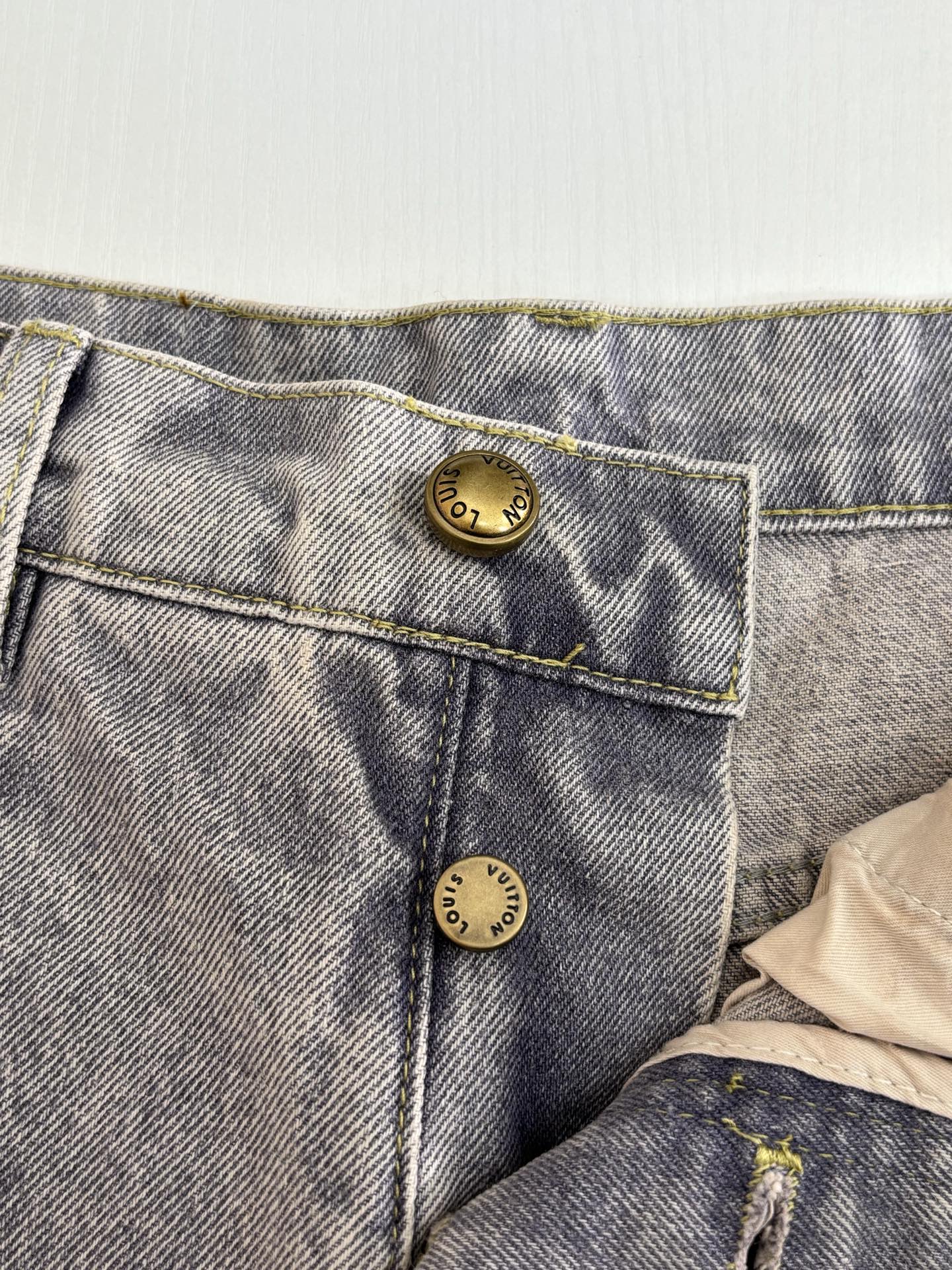 Close-up of light blue denim pants back pockets with gold-toned button accents
