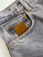 Close-up of light blue denim pants waistband with tan leather label and gold buttons
