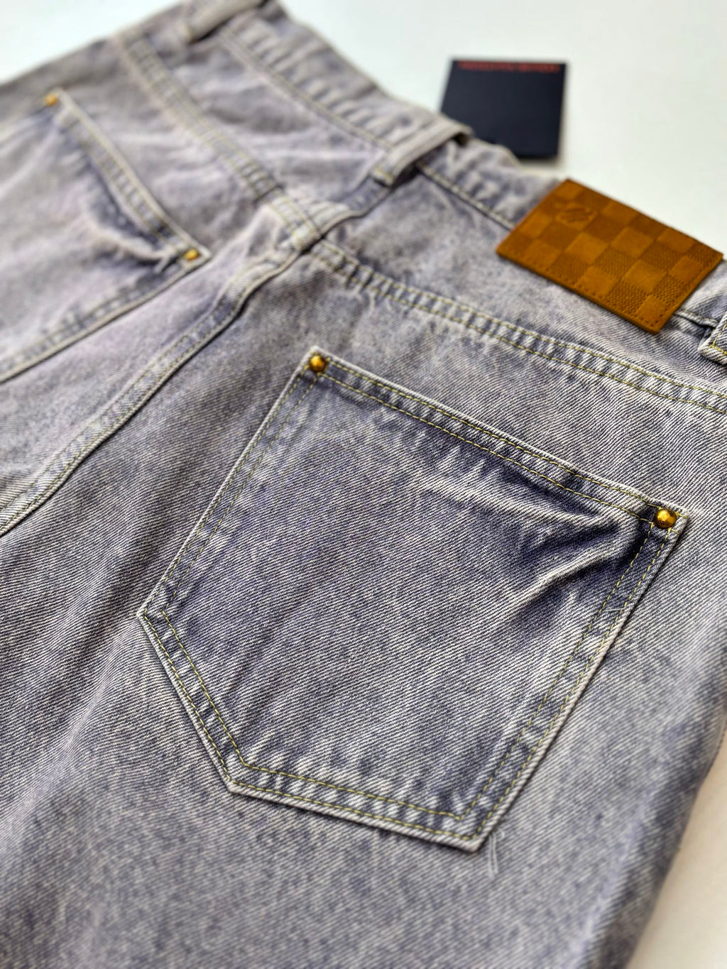 Light blue denim pants close-up with tan label and stitched front pocket edges