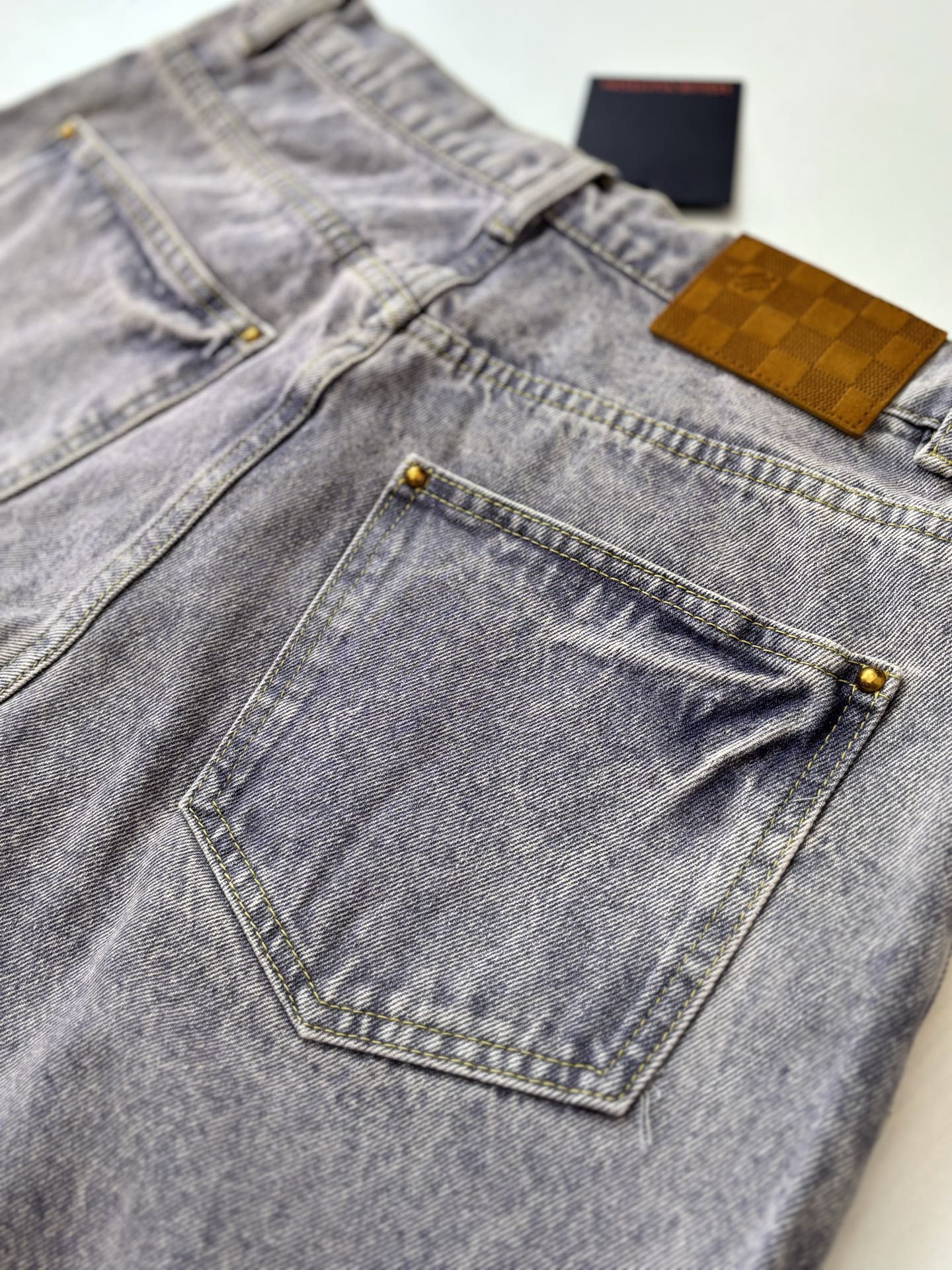 Light blue denim pants close-up with tan label and stitched front pocket edges