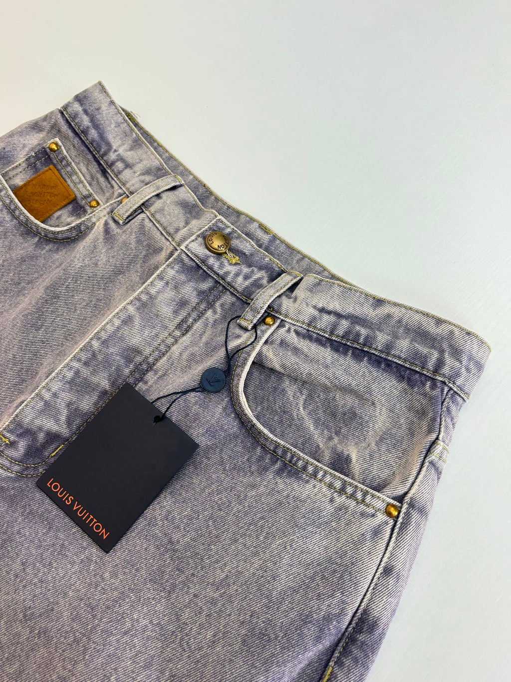 Light blue denim pants detail view with waistband, belt loops, and front button