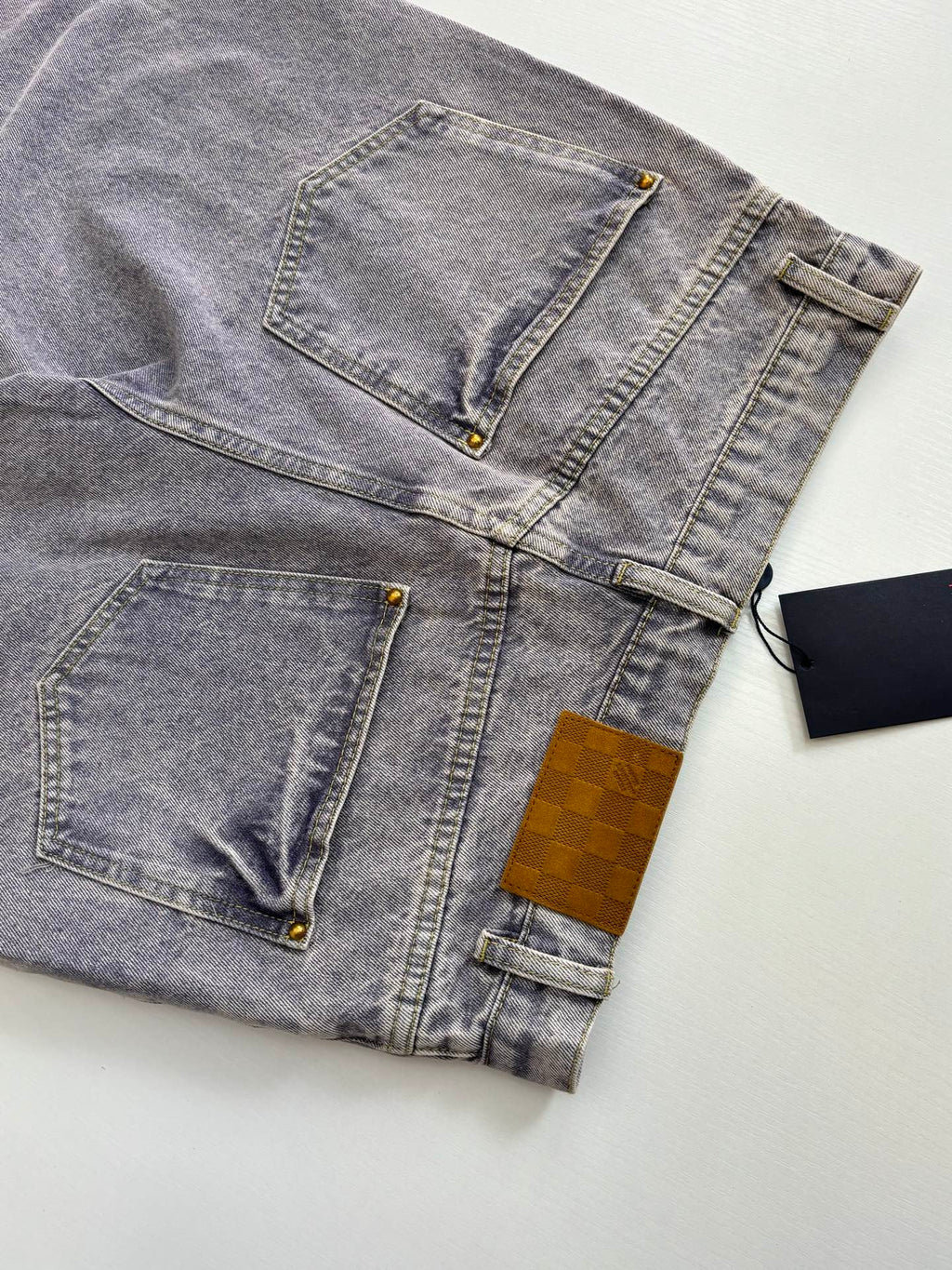 Light blue denim pants flat lay showing stitched pockets and gold button details