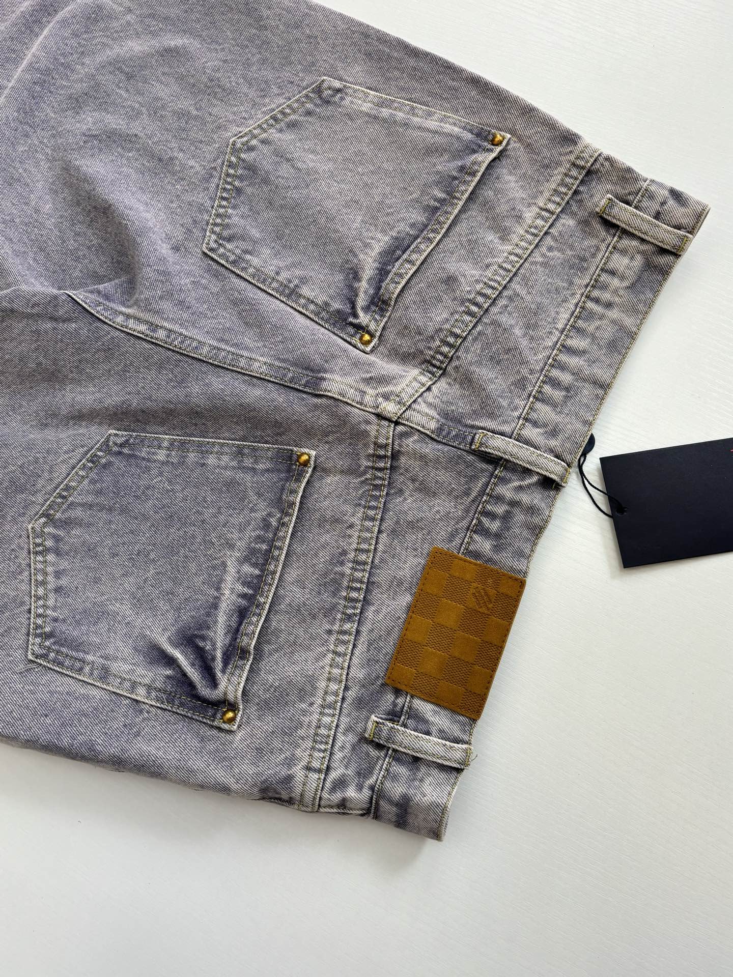 Light blue denim pants flat lay showing stitched pockets and gold button details